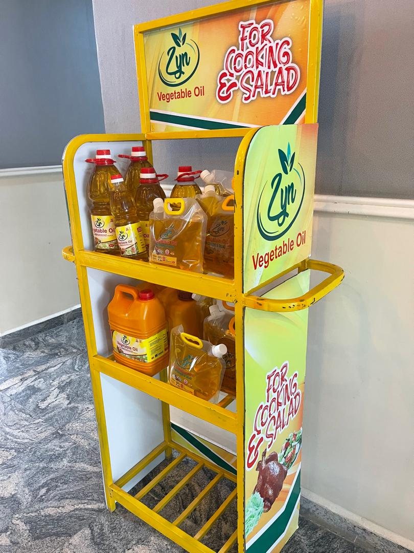 A yellow metal Zyn Vegetable Oil stand holding bottles, pouches and kegs of oil.