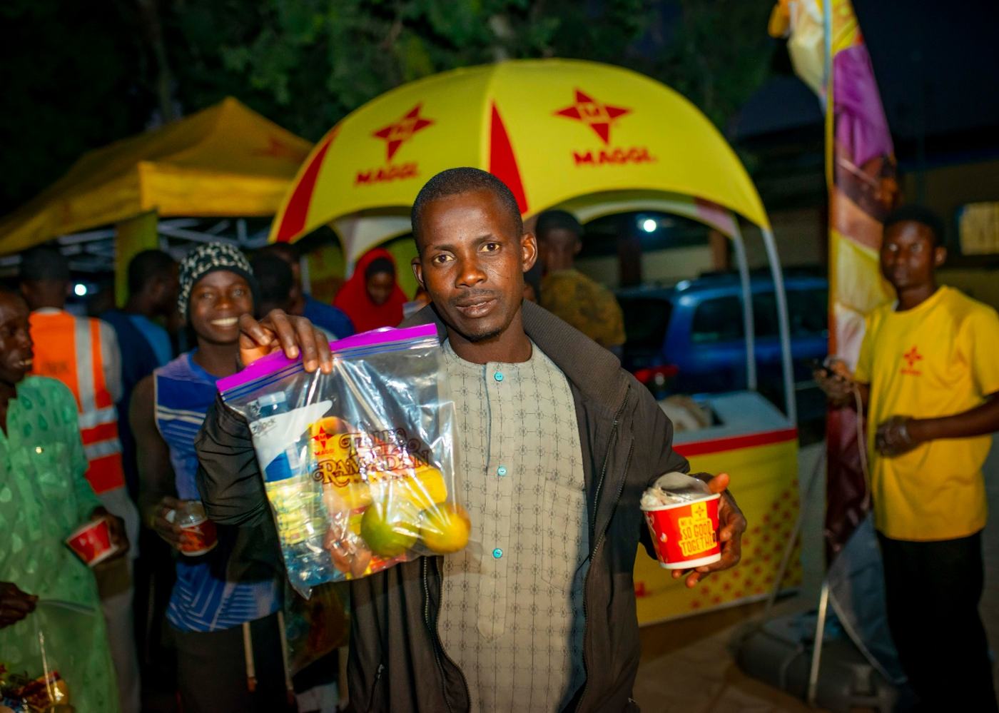 A man holding his iftar pack and a branded cup in front of the Maggi Star umbrella.