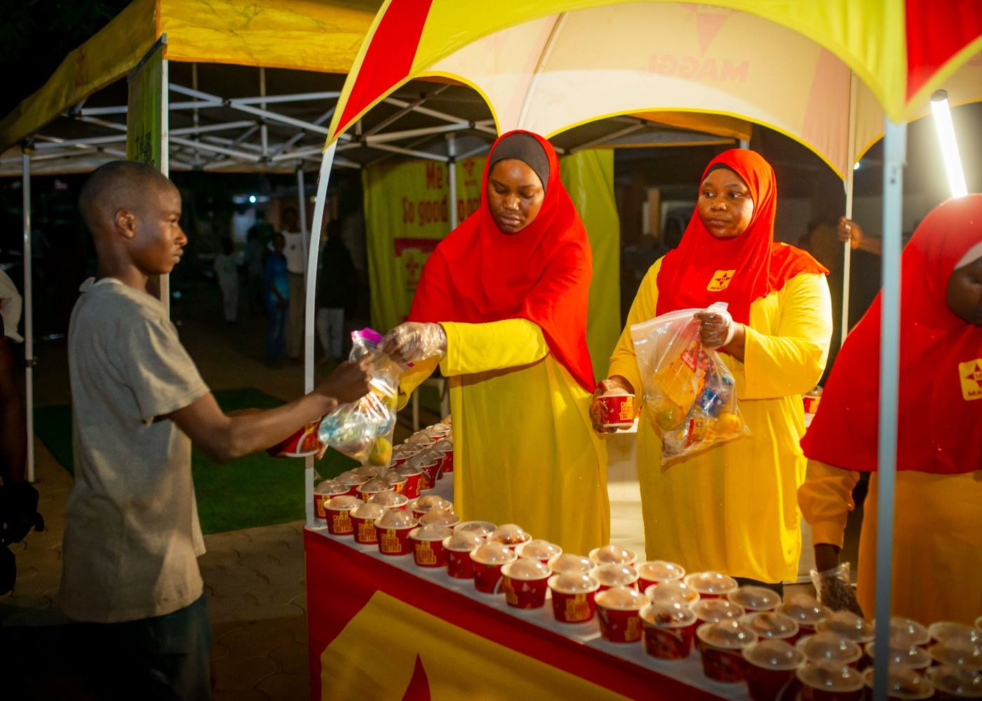 Brand ambassadors in red and yellow handing packs across the sampling counter.