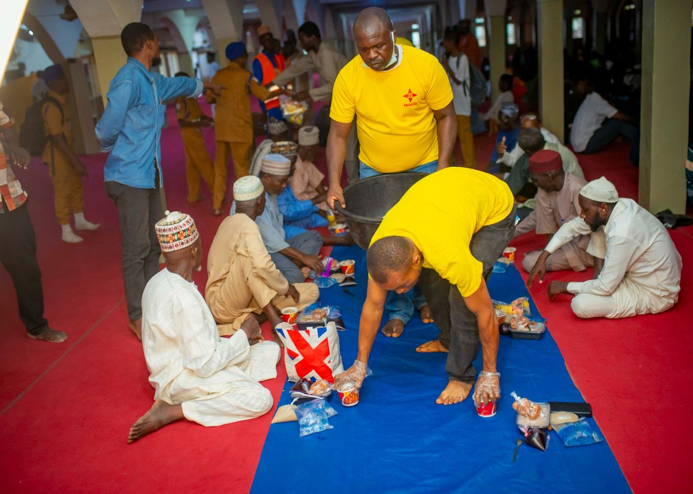 Field team serving guests seated for iftar inside the hall.