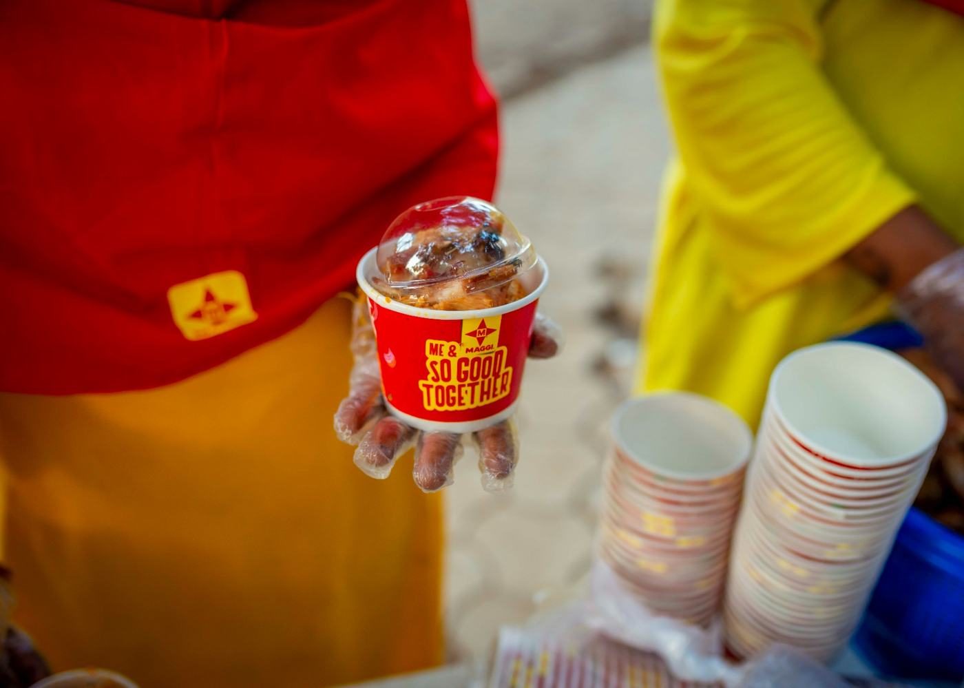 Close up of a gloved hand holding a branded portion cup beside stacks of empty cups.