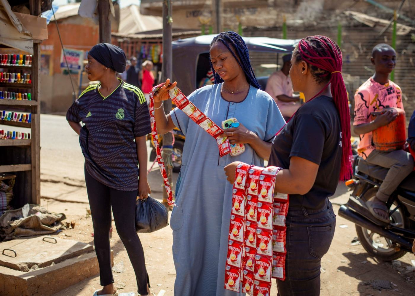 Two brand ambassadors offering Nescafe 3-in-1 sachet strips to a woman outside a kiosk.
