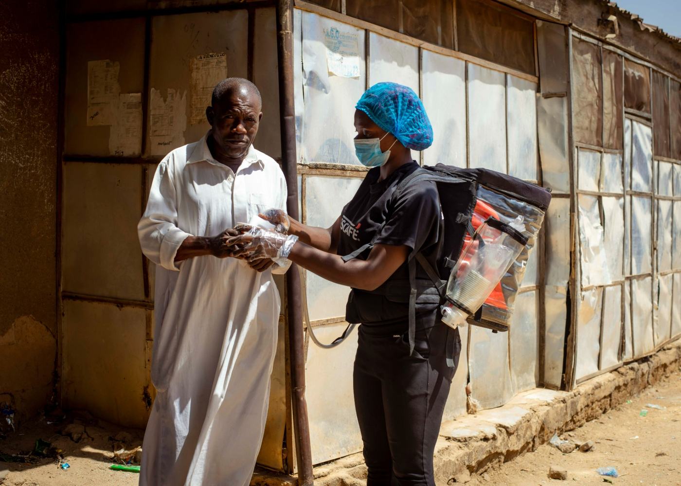 An ambassador with a backpack dispenser serving a hot cup of coffee to an older man.