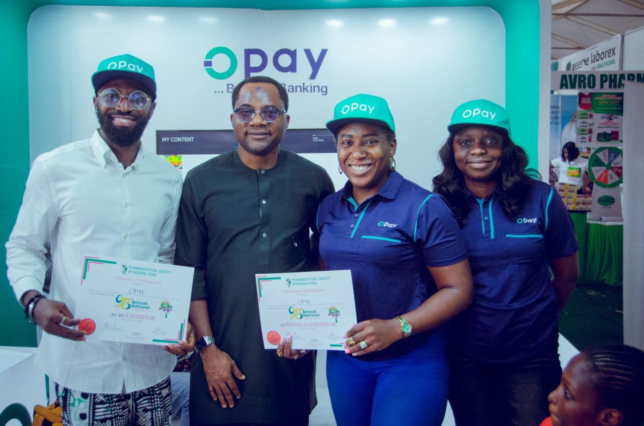 Four people holding OPay exhibitor certificates in front of the OPay stand.
