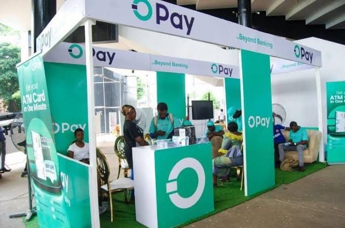 A green and white OPay exhibition stand with staff serving customers at counters.