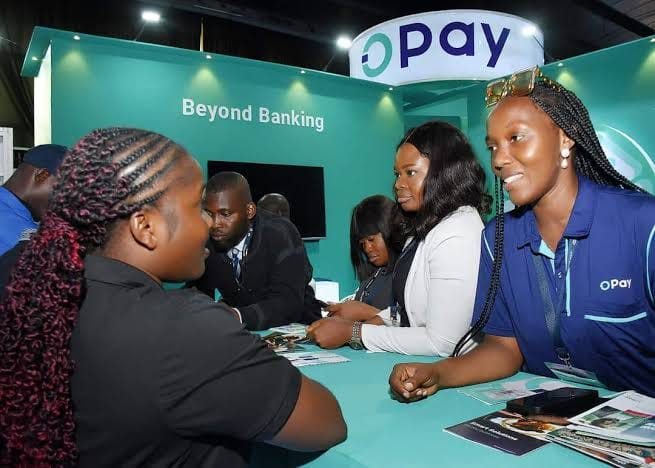 OPay staff in blue polos talking to visitors across a counter under a Beyond Banking wall.