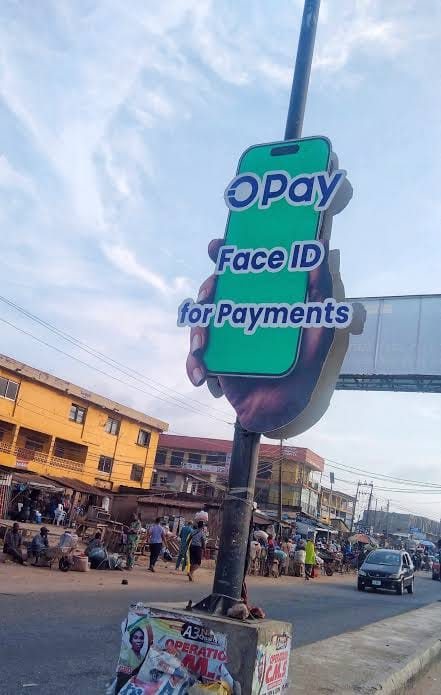 A shaped OPay cut out advert of a hand holding a phone, mounted on a pole above a street.