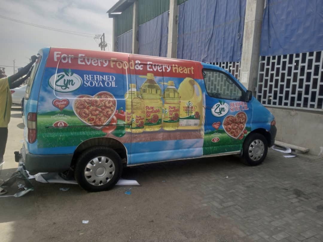 A blue van being wrapped with Zyn Refined Soya Oil artwork, offcuts on the ground.
